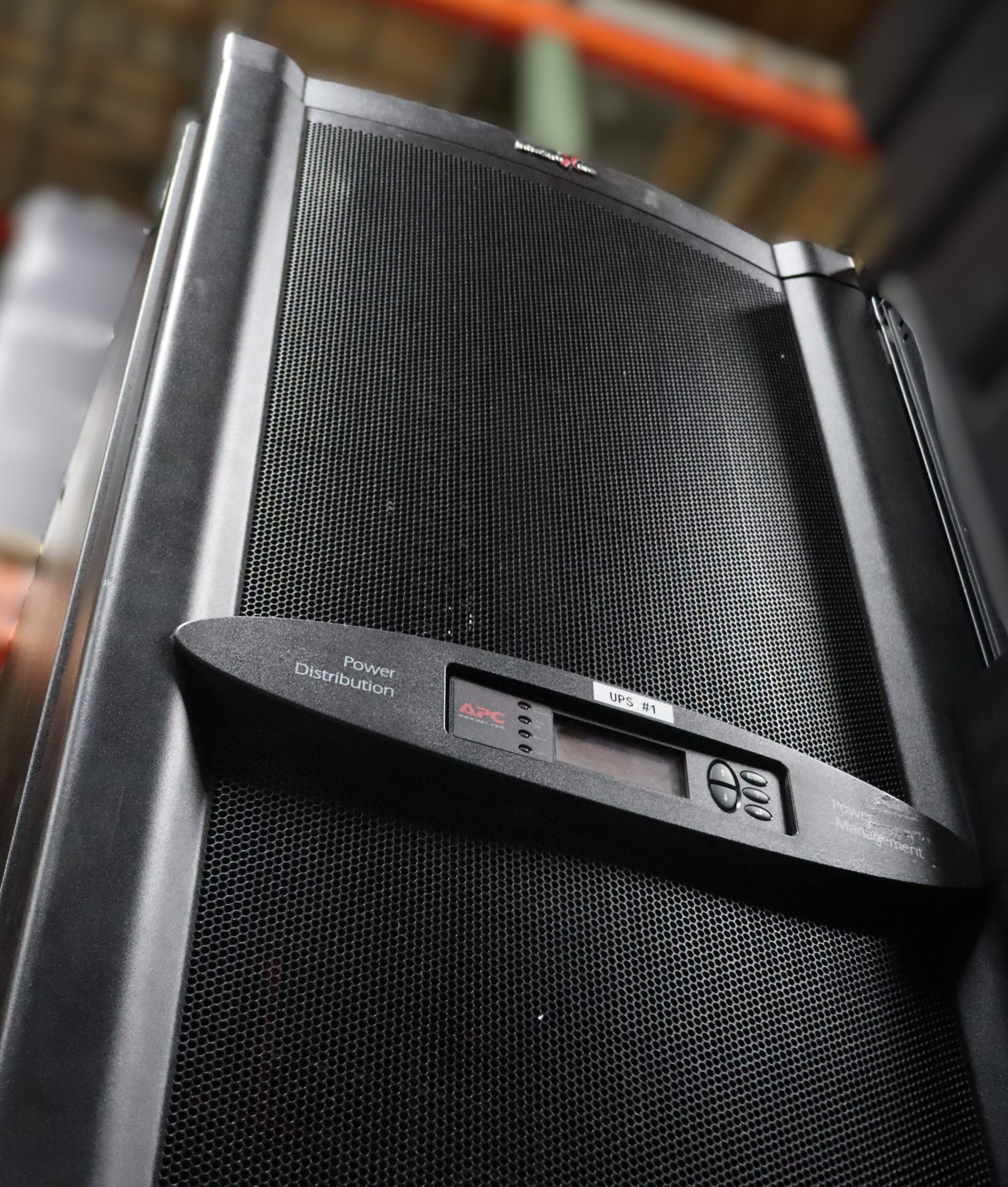 Black power distribution unit with a digital display and control buttons, set against a blurred industrial background.