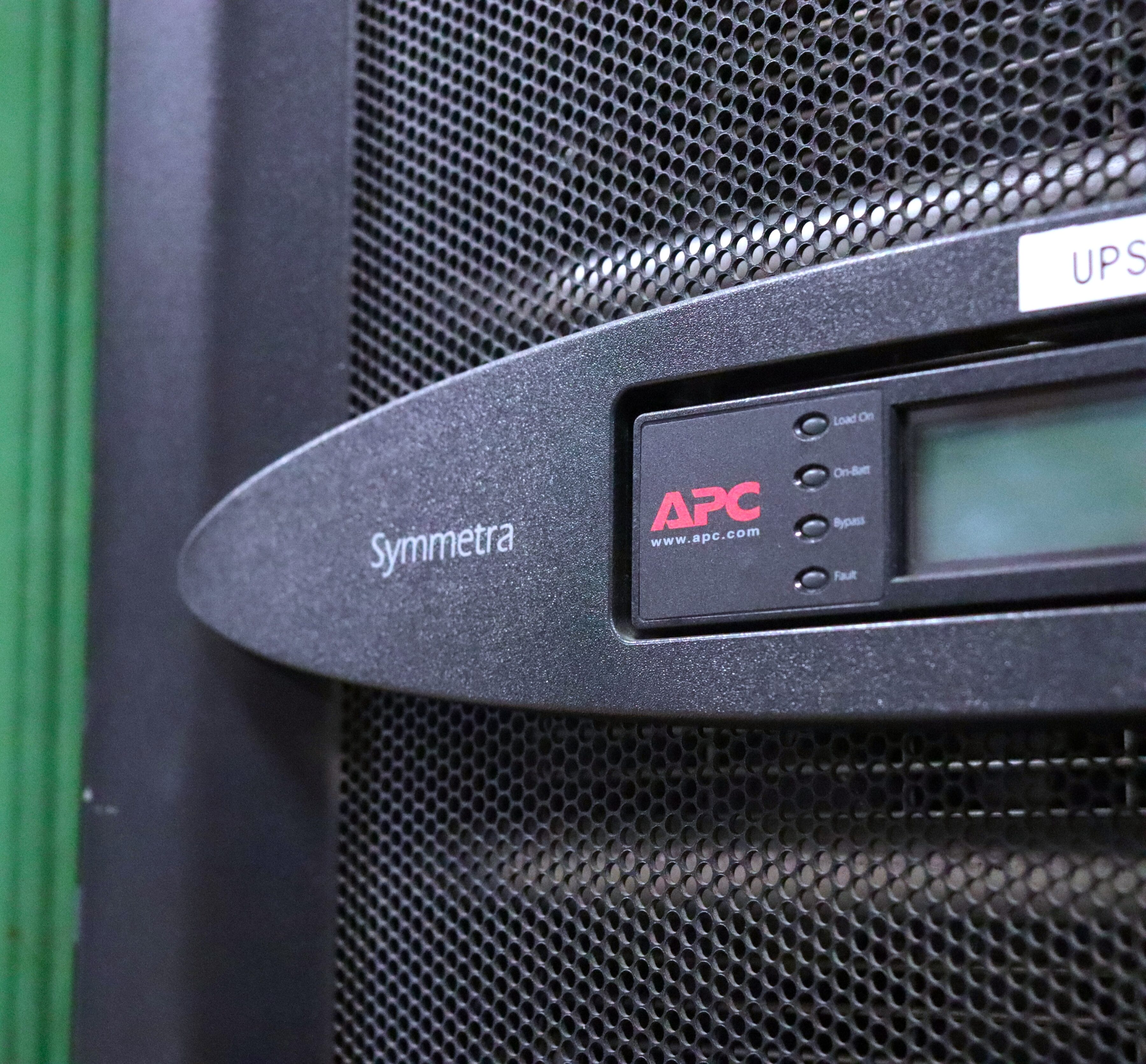 Close-up of an APC Symmetra UPS unit with a digital display and control buttons on a textured black surface.